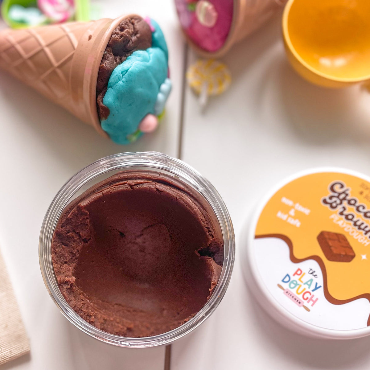 Chocolate play dough in a container with a cone and spoon on white table