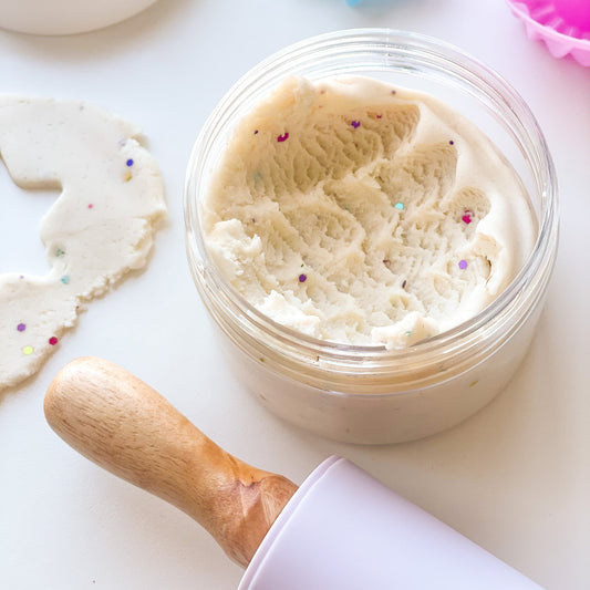 A jar of creamy white playdough with colourful glitter on a white background