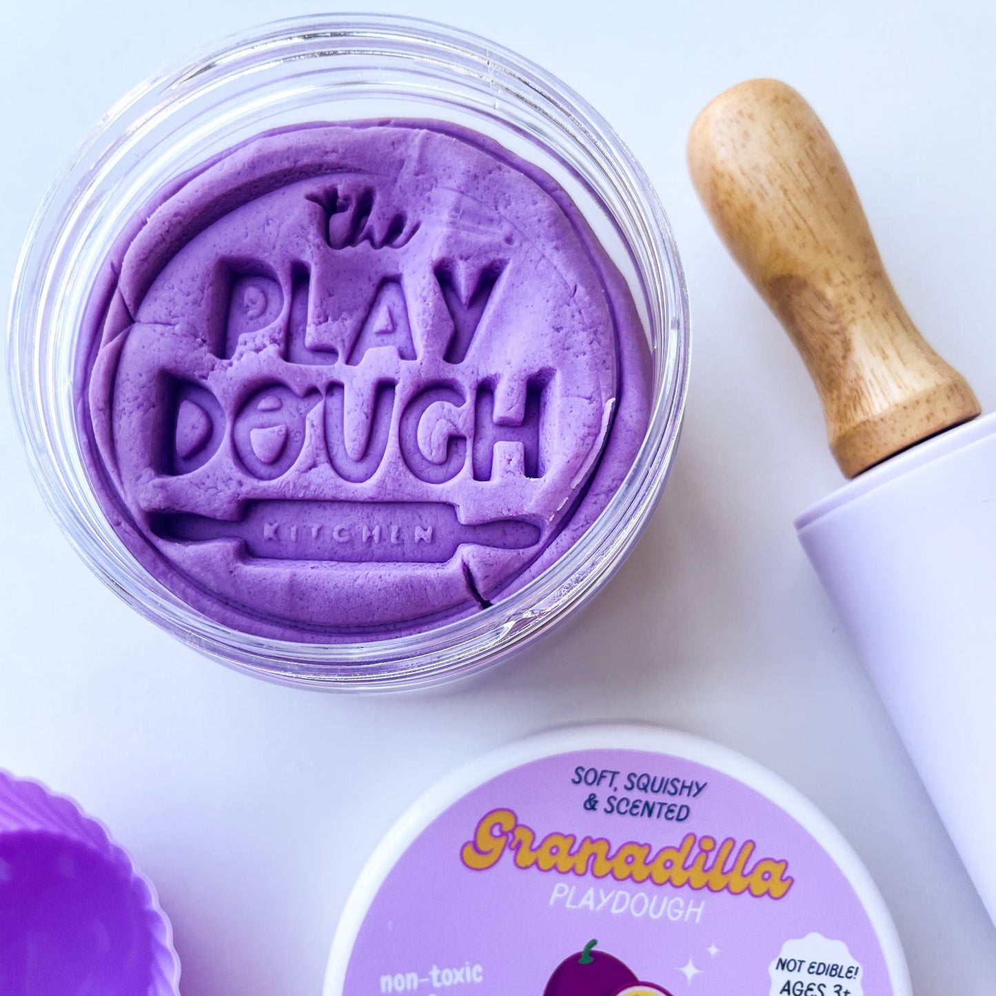 A jar of purple playdough stamped with the logo of The Playdough Kitchen