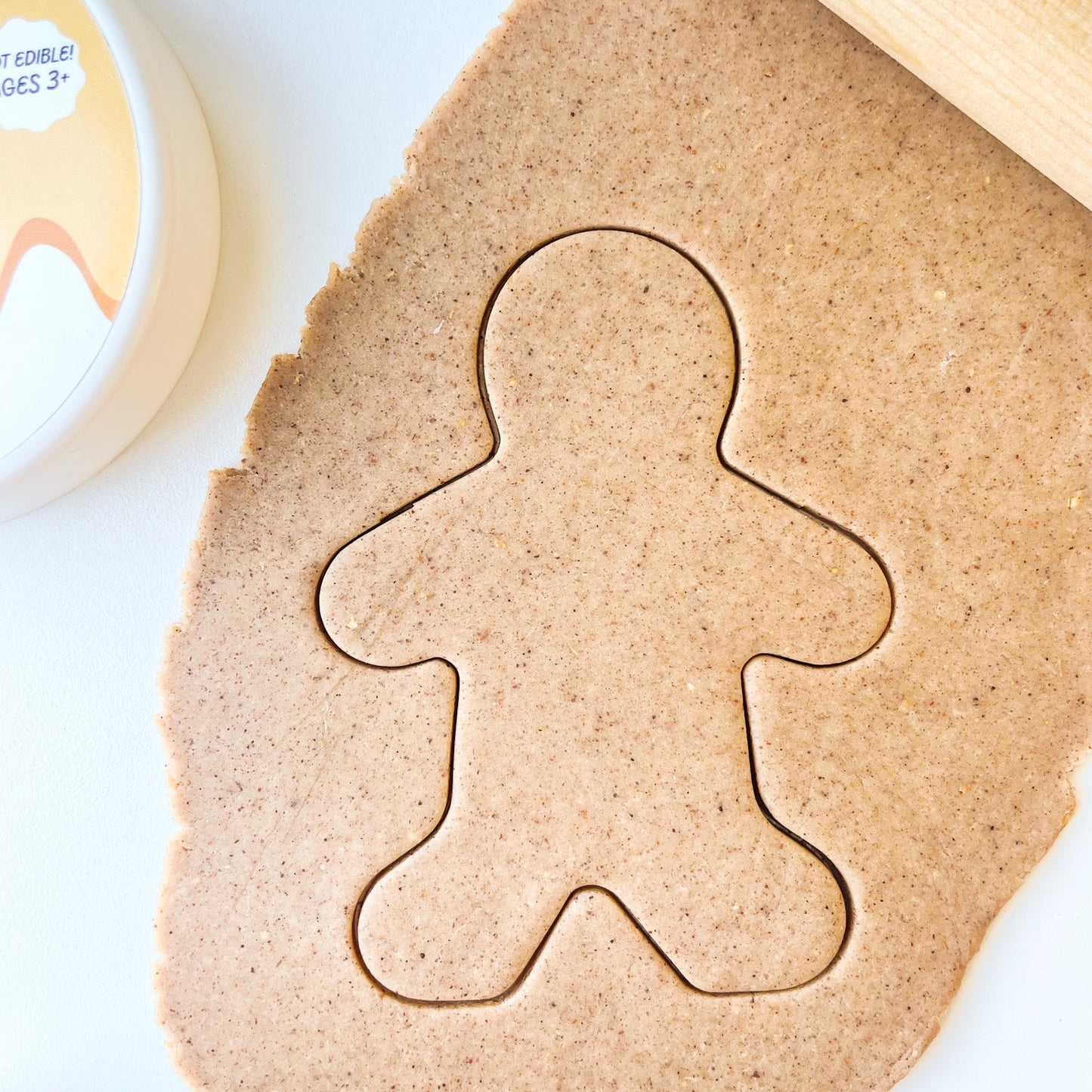 Gingerbread playdough rolled out onto a surface with a gingerbread man shape pressed into it