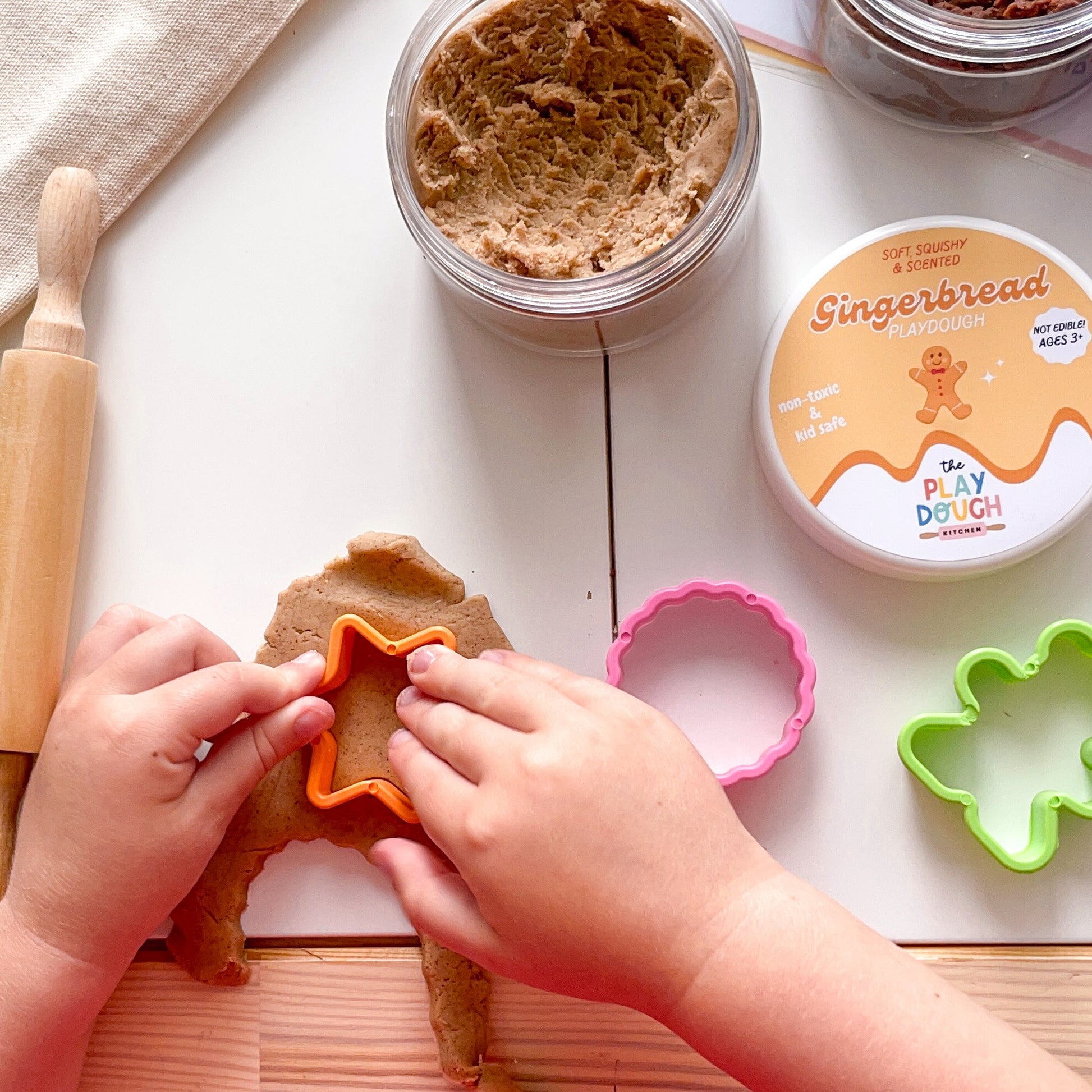 Child playing with gingerbread-themed play dough and tools on a white surface.