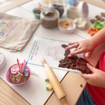 Child playing with play dough on a table with various play items.