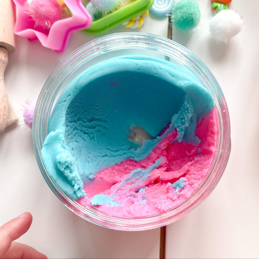 Colorful blue and pink bubblegum play dough in a container with tools on a light surface