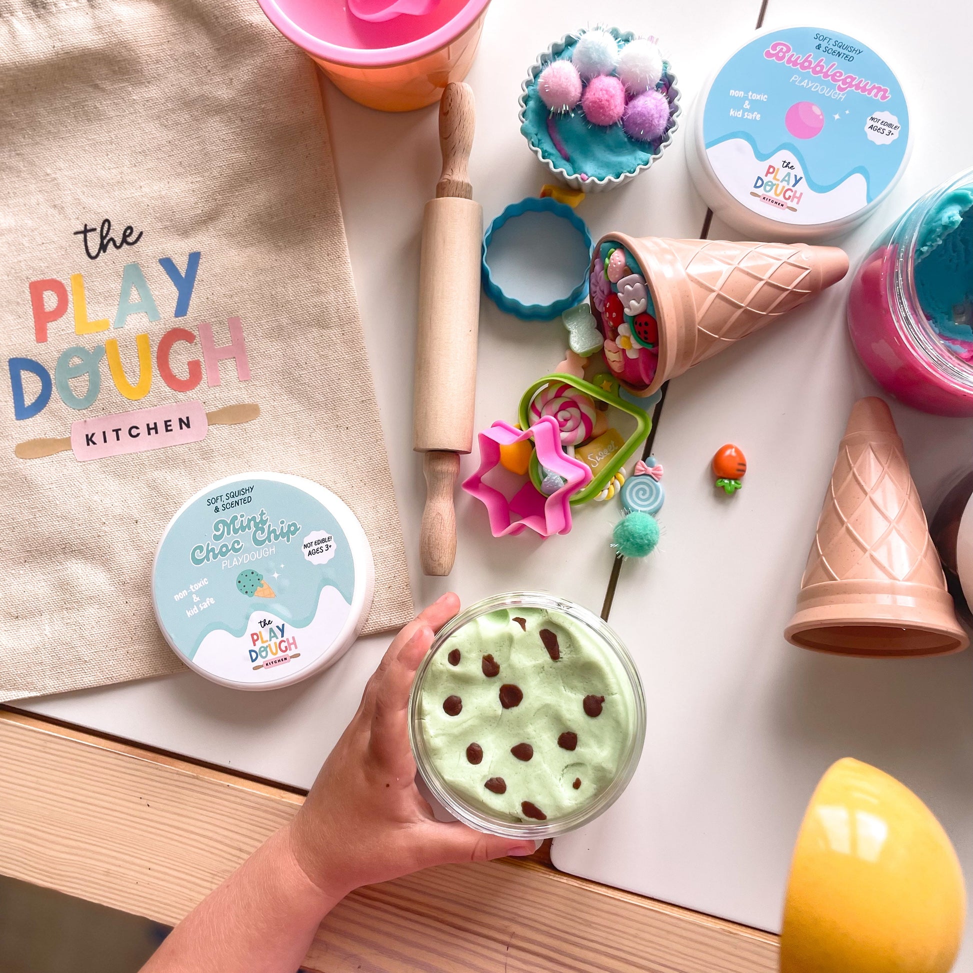 Play dough kit with containers, tools, and a child's hand holding a tub of mint chip play dough.
