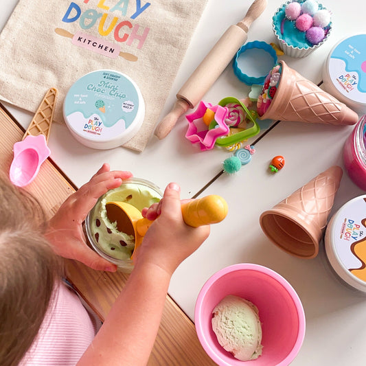 Child playing with play dough and kitchen toys on a table.