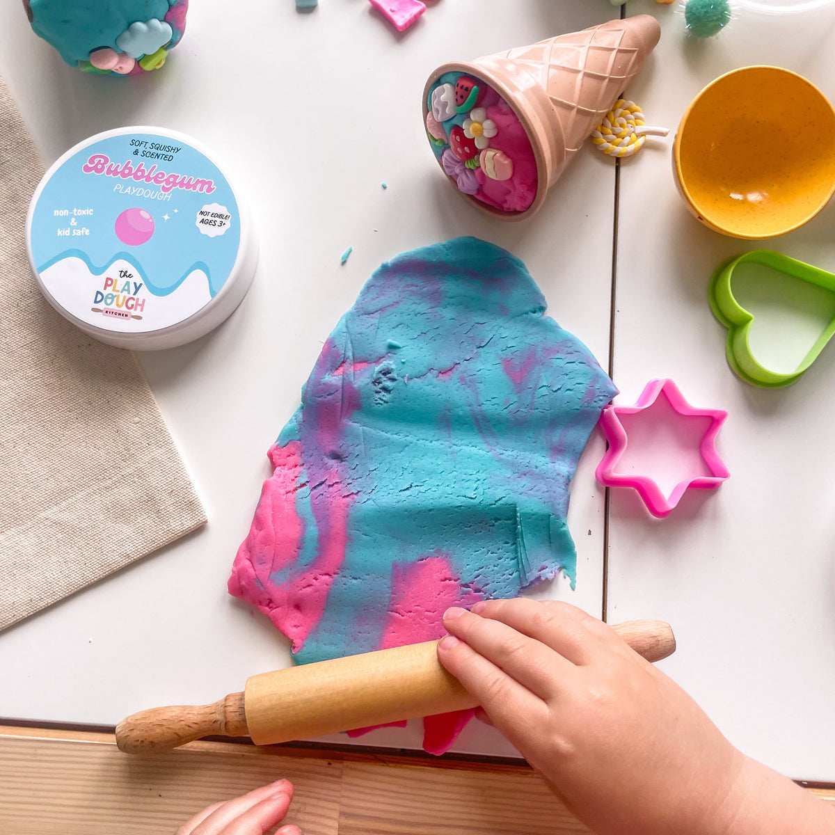 Bubblegum play dough with a rolling pin on a table, surrounded by play ice cream toys.
