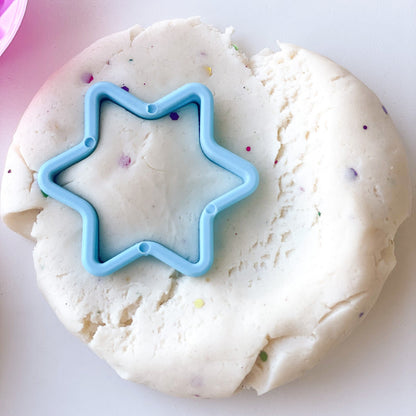Creamy white play dough with colourful glitter and a blue star cookie cutter pressed into it.