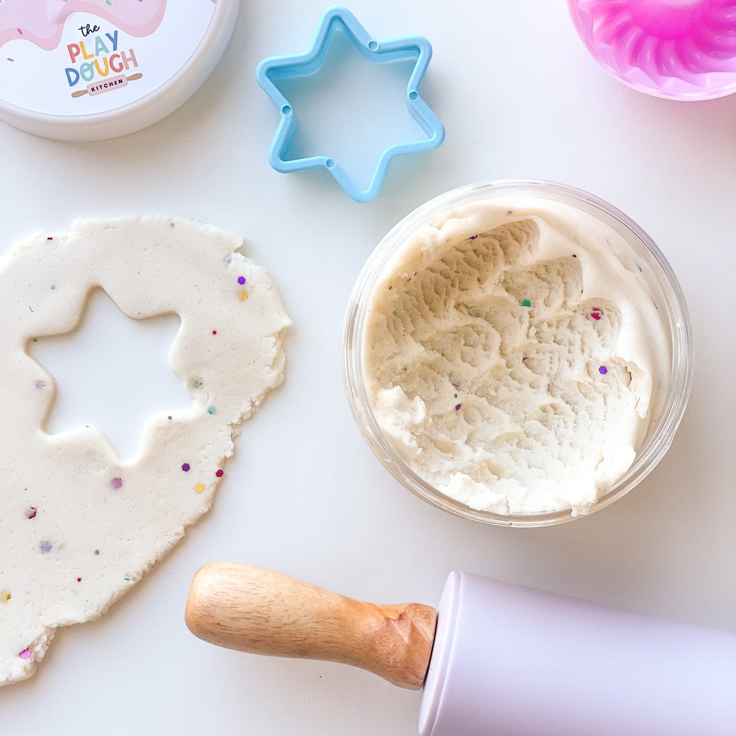 A jar of creamy white playdough with colourful glitter on a white background