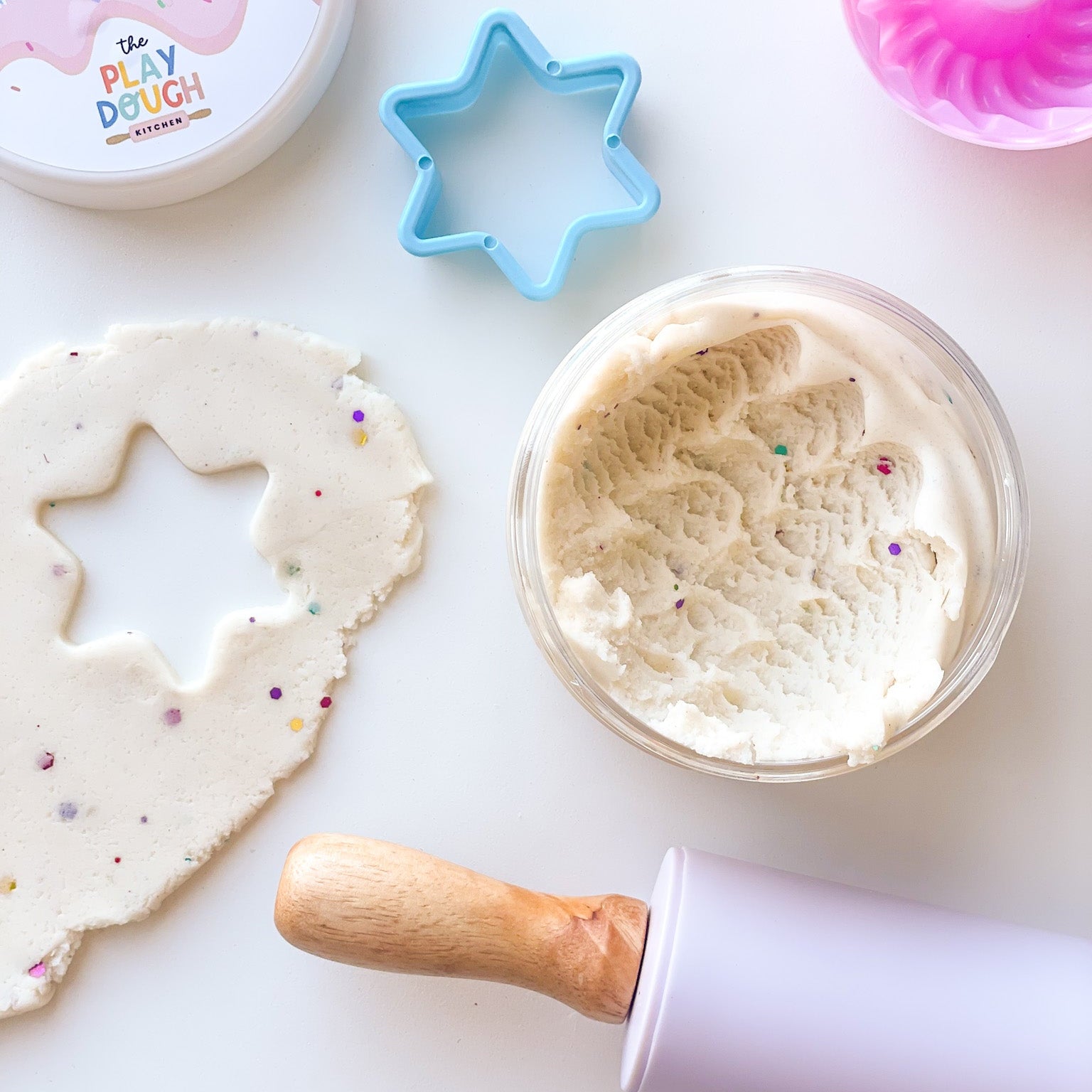 A jar of creamy white playdough with colourful glitter on a white background