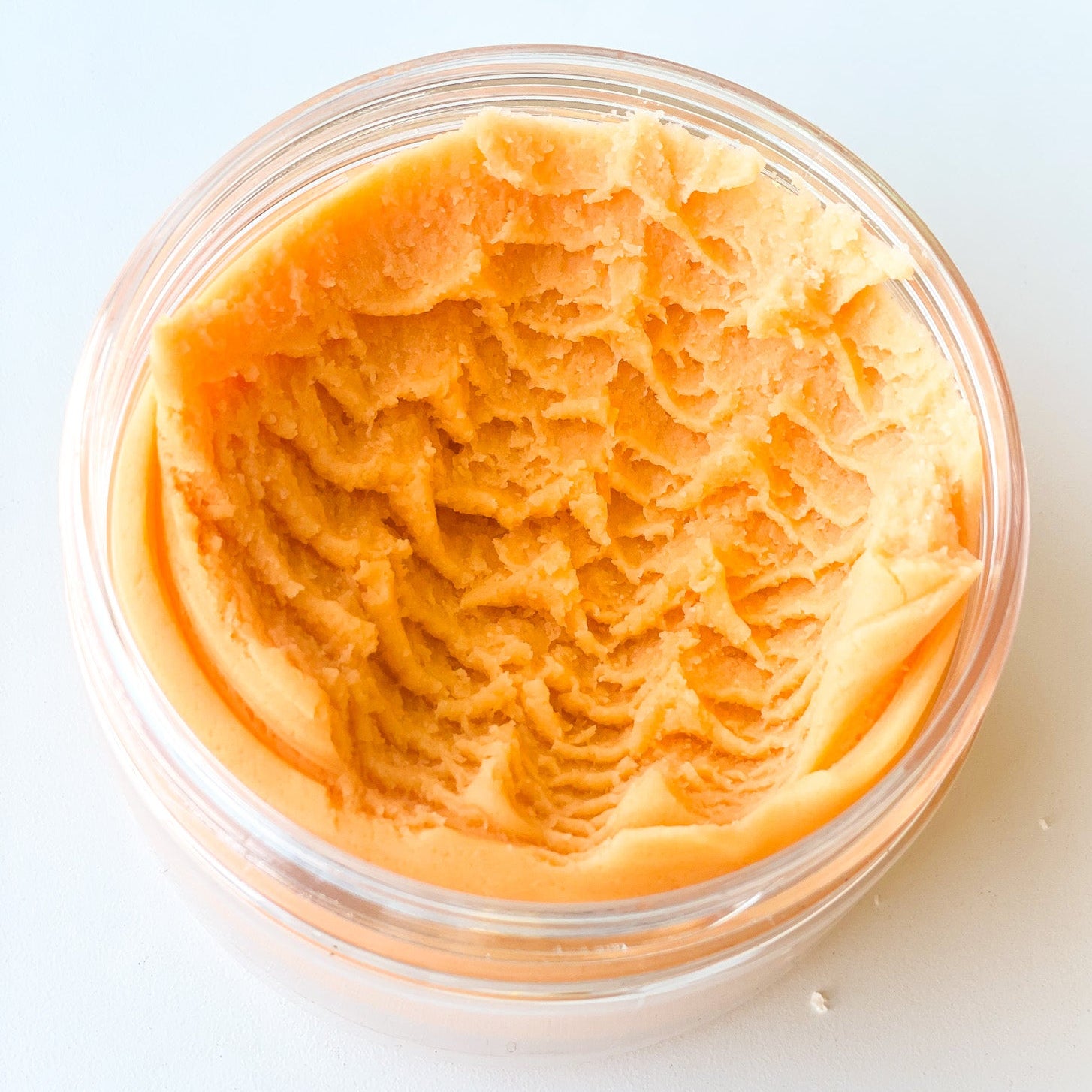A clear jar full of orange play dough on a white surface