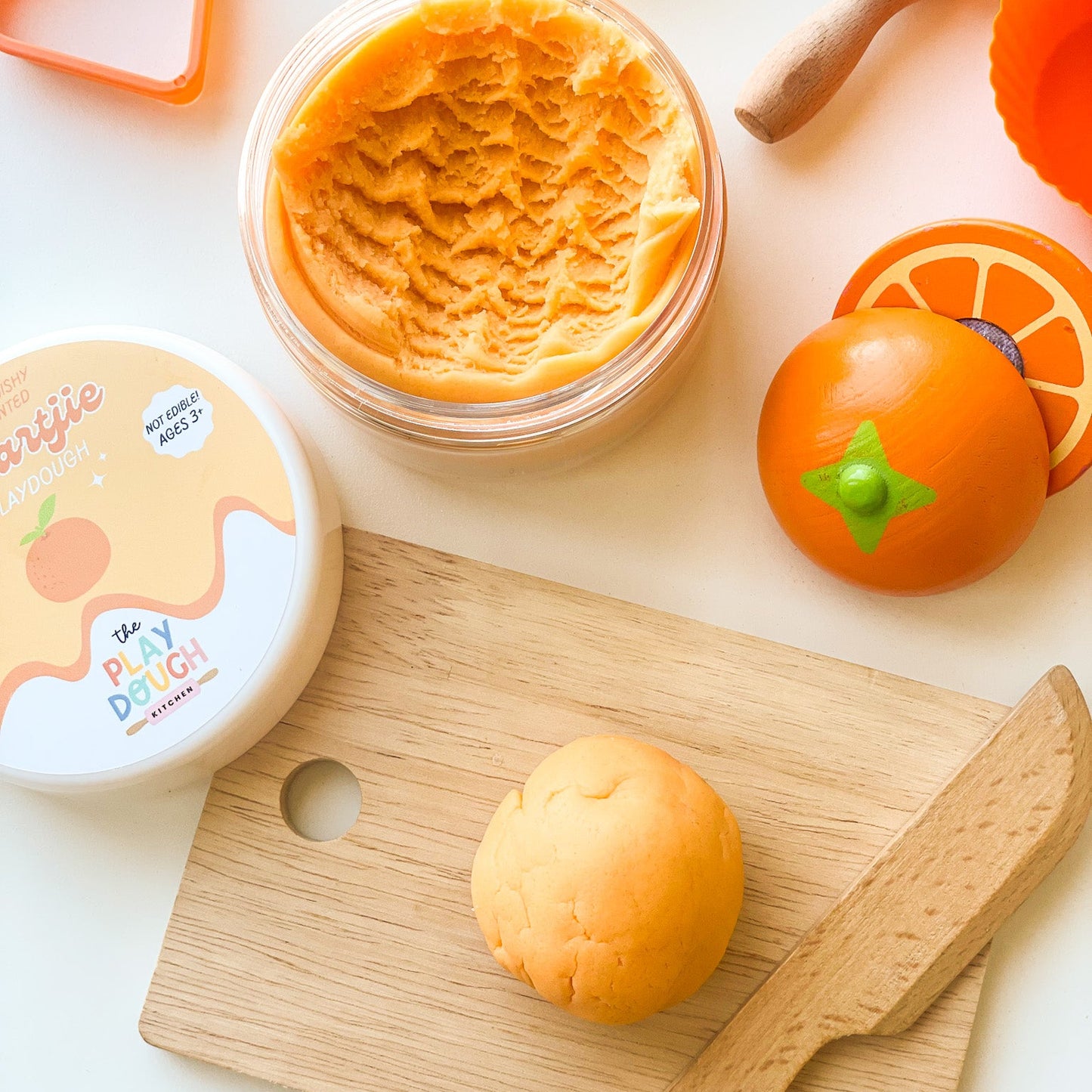Orange playdough with wooden chopping board and knife on a white background