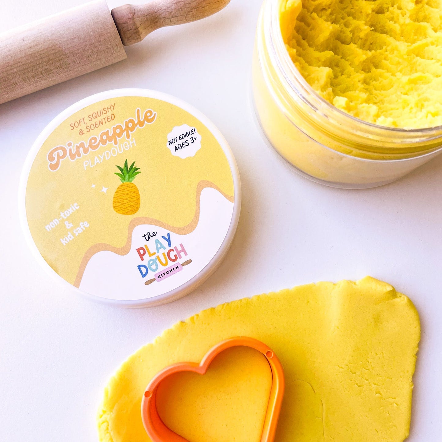 Yellow pineapple playdough rolled out onto a white surface with an orange cookie cutter