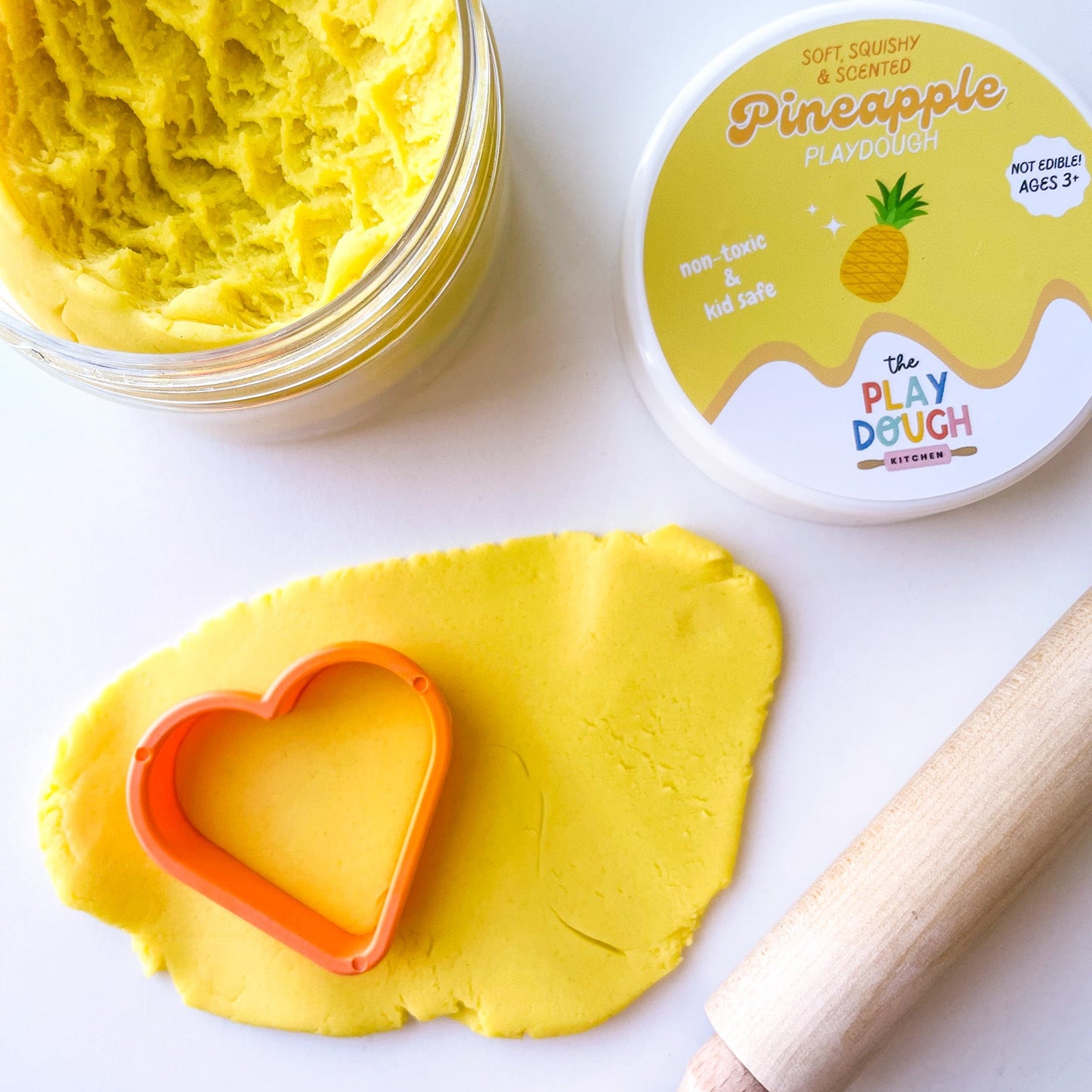 Yellow play dough with a heart-shaped cutter and rolling pin on a white background