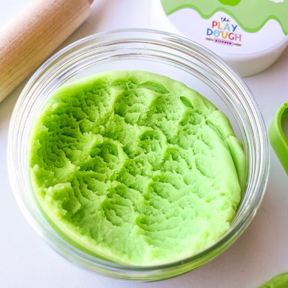 Green apple playdough in a clear jar on a white surface