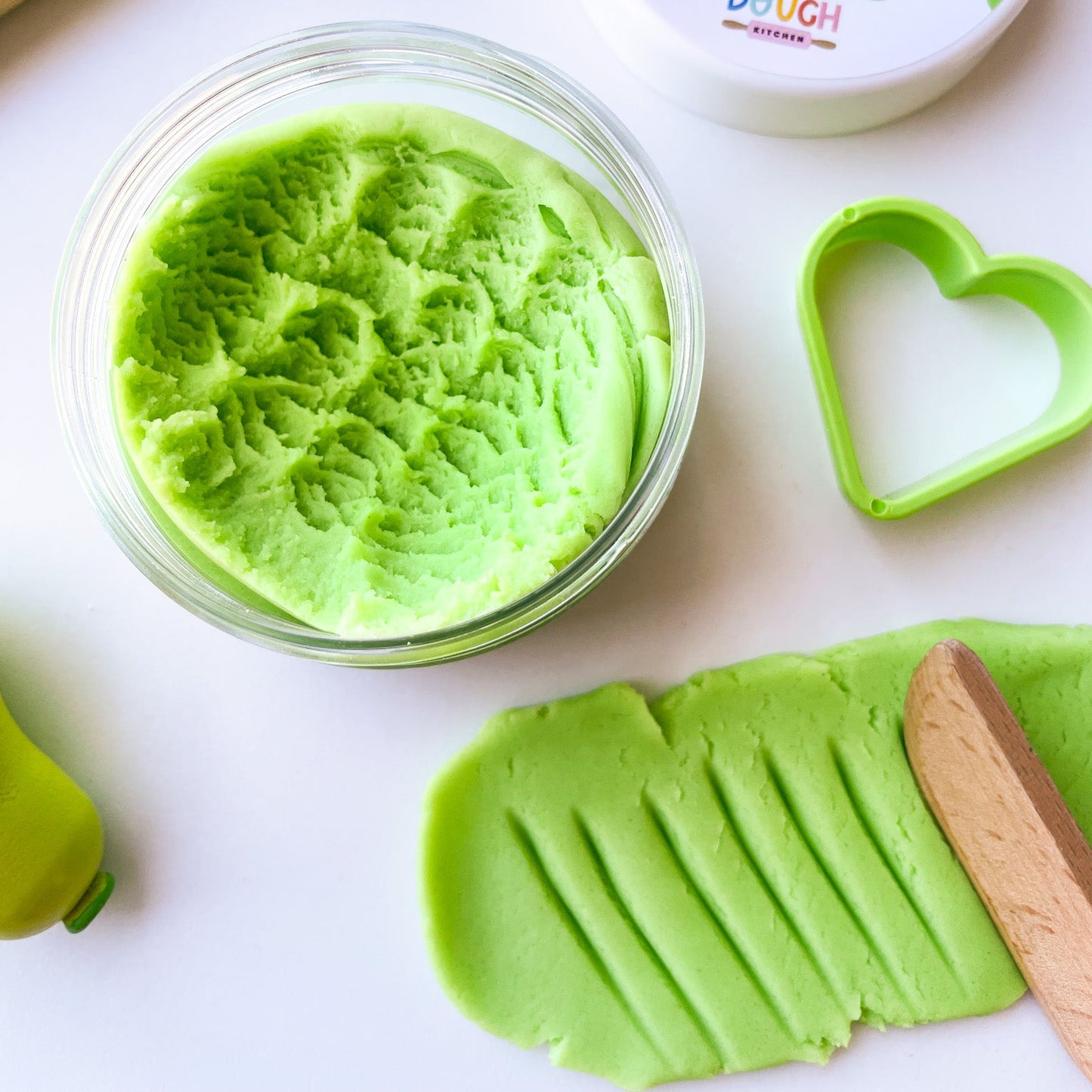 Green apple playdough in a clear jar with tools on a white background