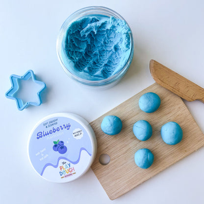 Blue play dough with a tub with a wooden board, and cookie cutter on a light background