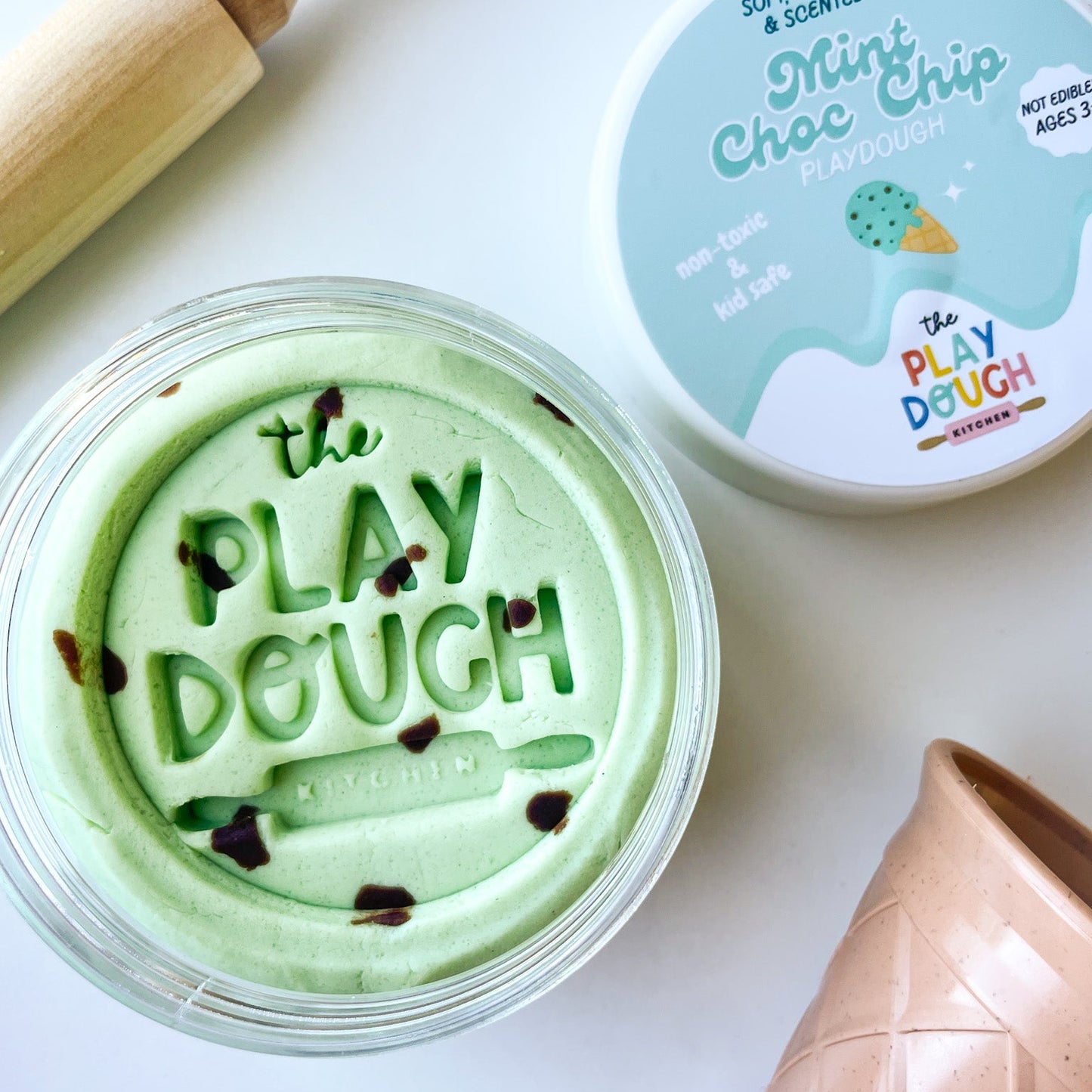 Green play dough in a container with a rolling pin and ice cream cone on a white background